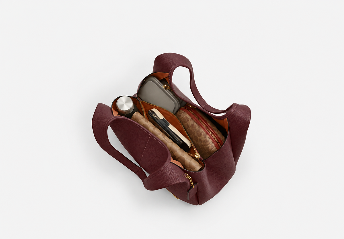 Burgundy tote bag holding a bottle, pouches and everyday essentials around its central zip compartment.