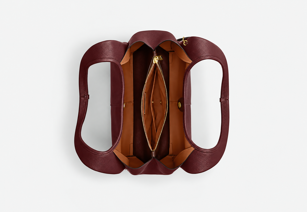 Open burgundy tote bag showing tan lining, a central zip compartment and snap closure.