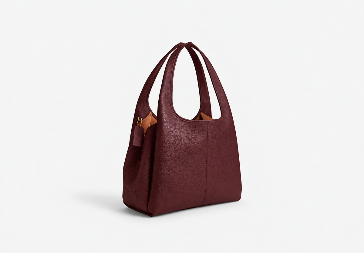 Burgundy pebble leather tote bag viewed at an angle, showing the side panel and hanging tag